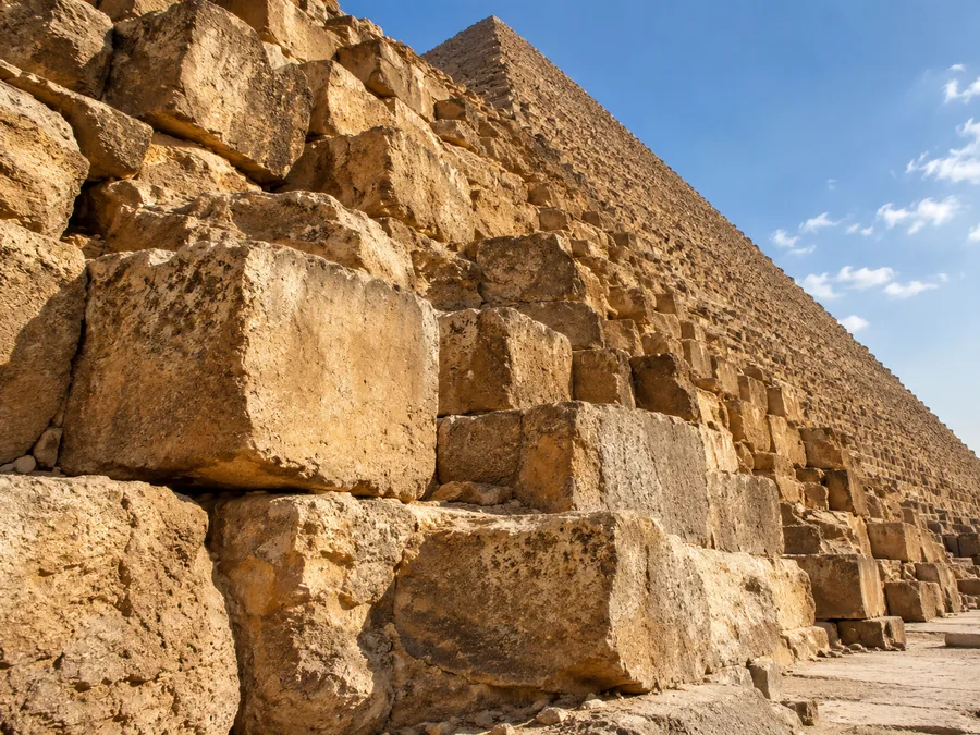 الكتل الضخمة من الحجر الجيري المتآكل عند قاعدة الهرم الأكبر في ضوء جانبي دافئ